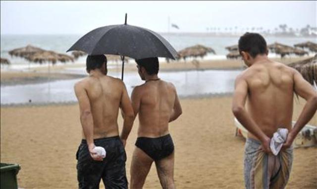 يحتمون من المطر بمظلة في ثياب السباحة أيلول 2011 - أرشيف
