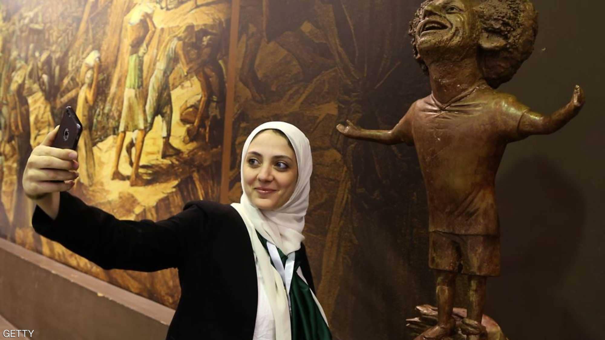   إحدى المشاركات في منتدى شباب العالم مع تمثال صلاح