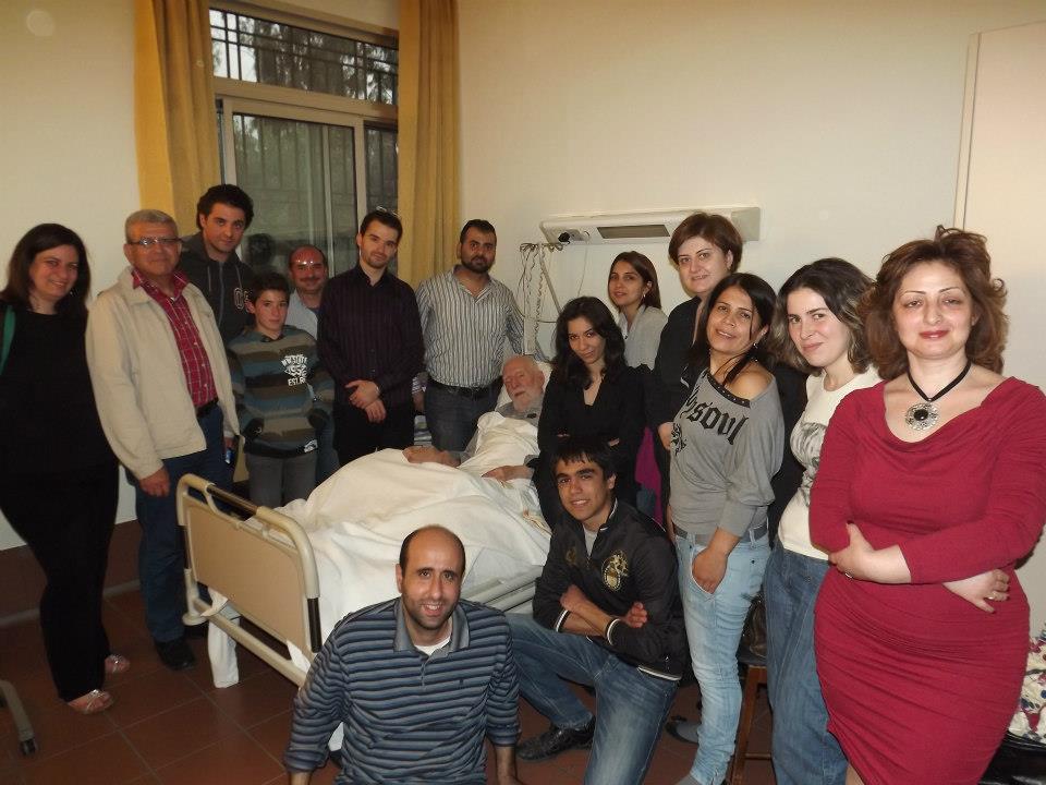 على اليمين هدى الجلبوط وفي أسفل الصورة المحامي باسل عبدالله وبعض محبي المطران يحيطون به يغمرونه بمحبتهم