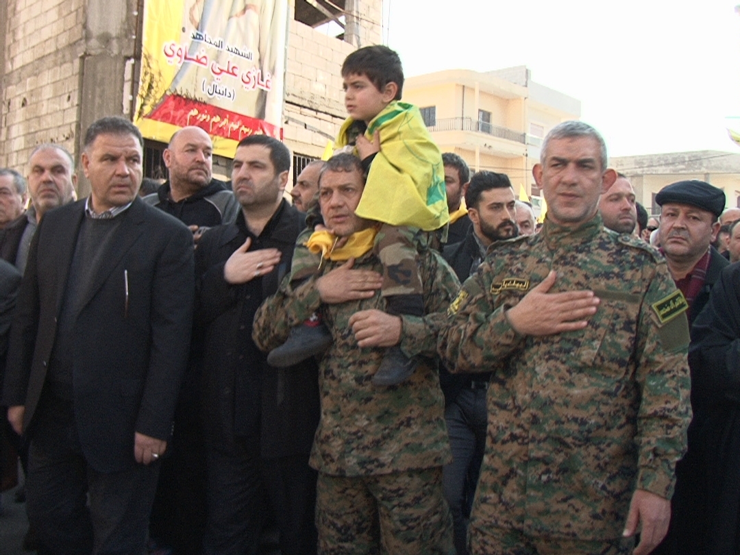 علي ضاوي (والد الشهيد) يحمل طفلاً، يتوسط الحاج إيهاب (عمّ الشهيد) والنائب علي فياض