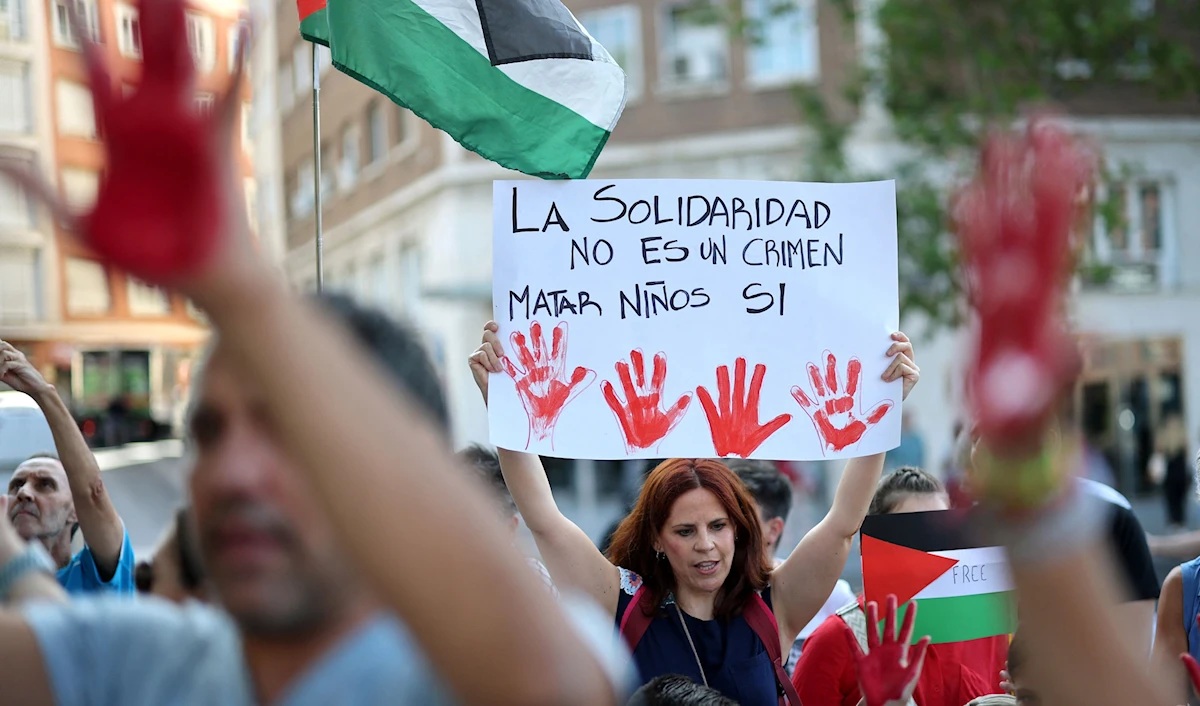متظاهرة تحمل لافتة كُتب عليها «التضامن ليس جريمة، قتل الأطفال هو الجريمة» خلال تظاهرة أمام السفارة الإسرائيلية في مدريد (أ ف ب)