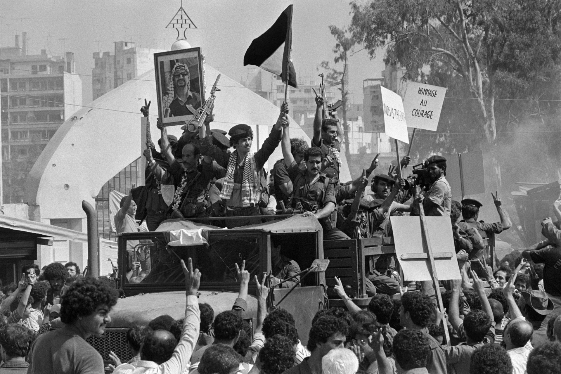 جنود منظمة التحرير الفلسطينية، حاملين صورة زعيمها ياسر عرفات، يحيون الحشود أثناء مغادرتهم بيروت، 30 أغسطس 1982 (أ ف ب)